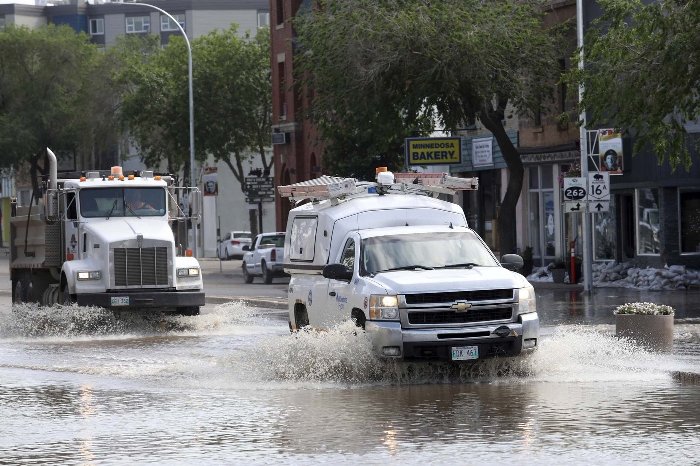 Vehicles pass through flood water on Main Street in Minnedosa on Monday after heavy downpours Sunday evening into overnight caused widespread flooding. The swollen Little Saskatchewan River overflowed into downtown Minnedosa flooding several businesses and residences. (Tim Smith/The Brandon Sun)
