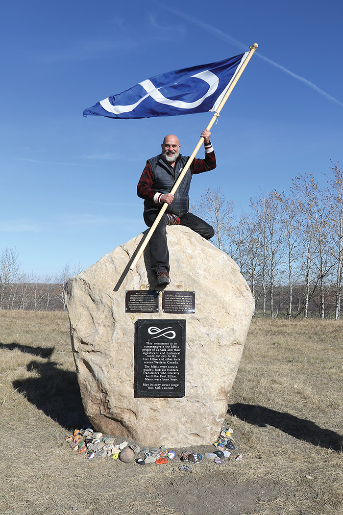 Will Goodon, Minister of Housing and Property Management of Manitoba Mtis Federation (MMF) Southwest Region holding the Mtis flag on the monument.