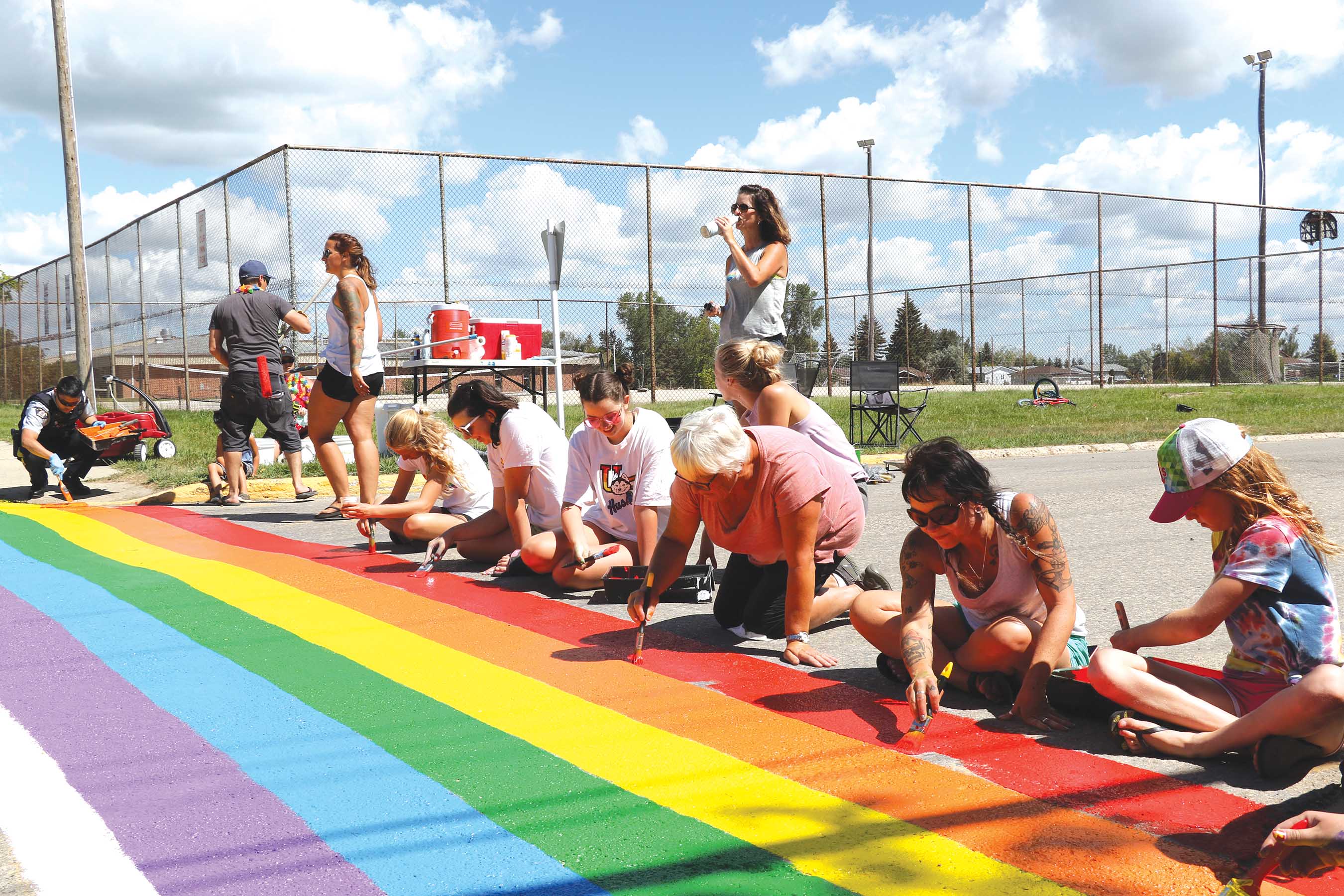 Volunteers painting a rainbow crosswalk in Redvers last year. The project brought lots of community members out, including the local RCMP who helped paint and wore RCMP vests with rainbow letters that day.