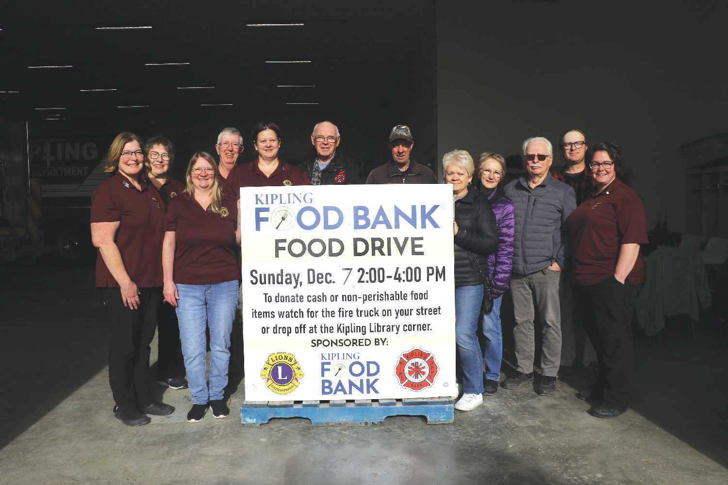 The Kipling Lions, Kipling Fire Department, and Kipling Food Bank posing with one of the signs that will go up in Kipling to get people ready for the Food Drive on December 7.